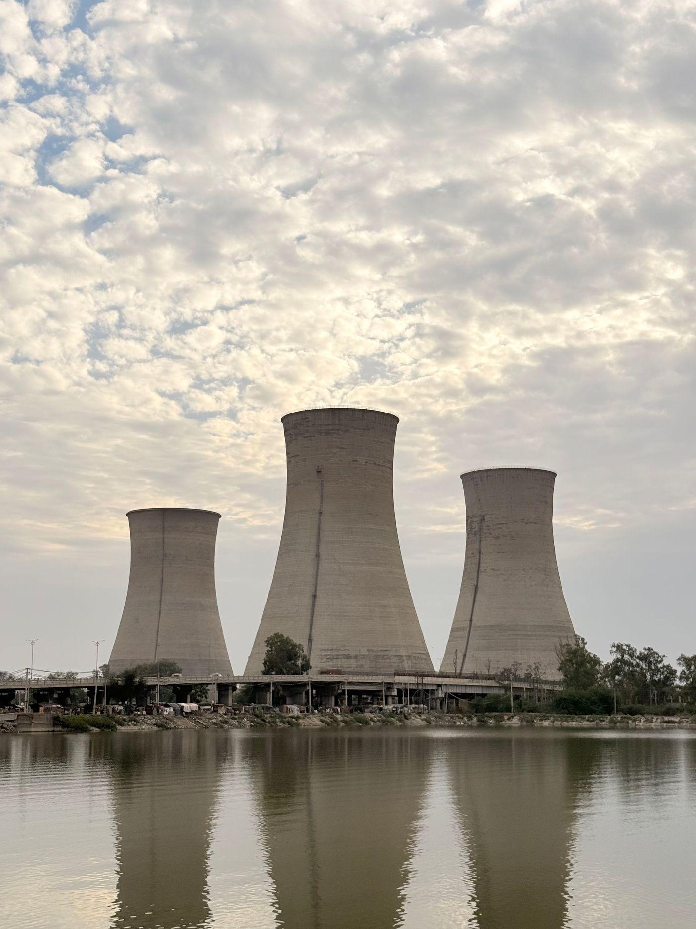 Industrial cooling towers reflected in still water beneath a heavy sky