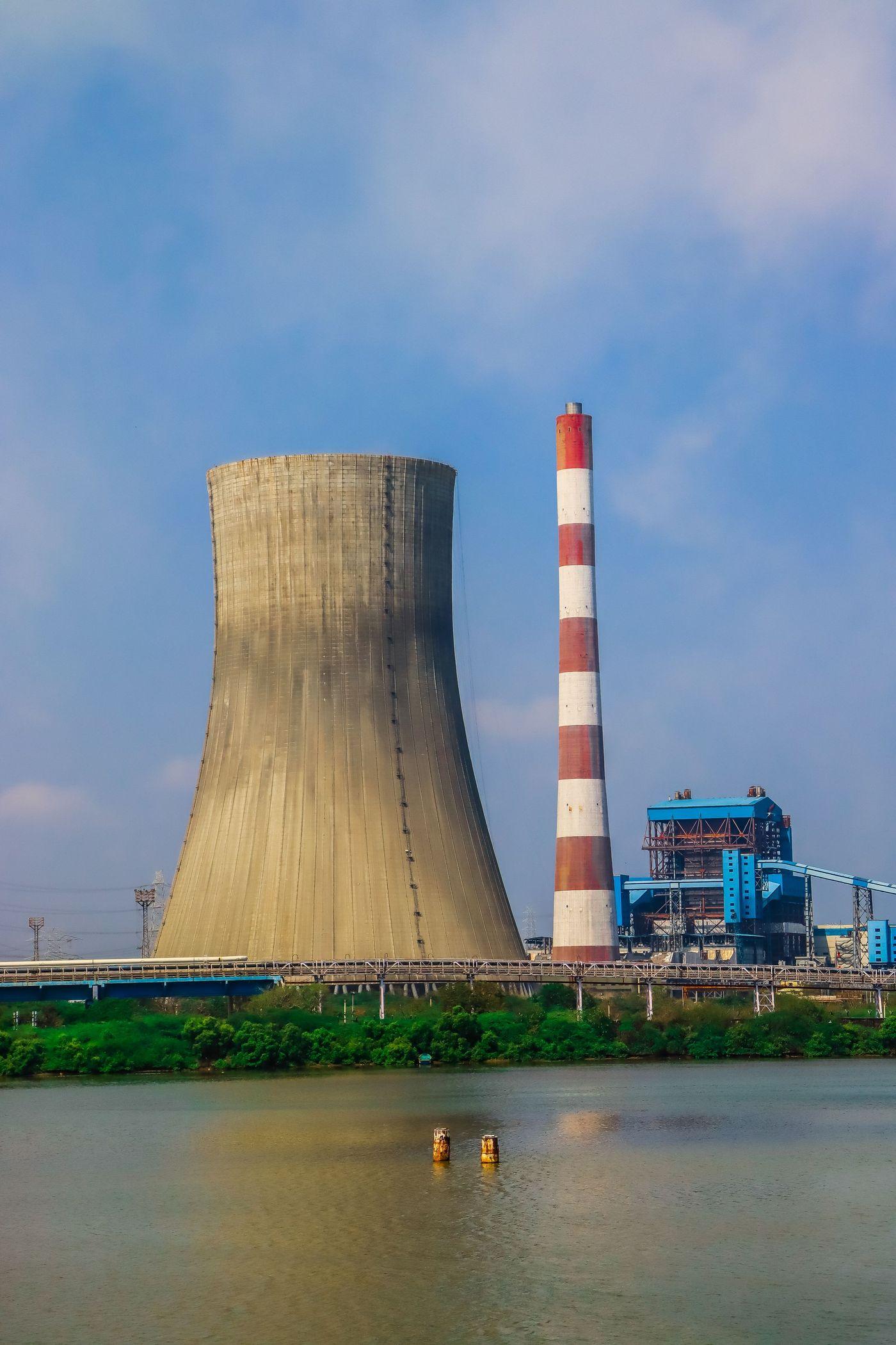 An industrial power plant with a cooling tower standing beside a river